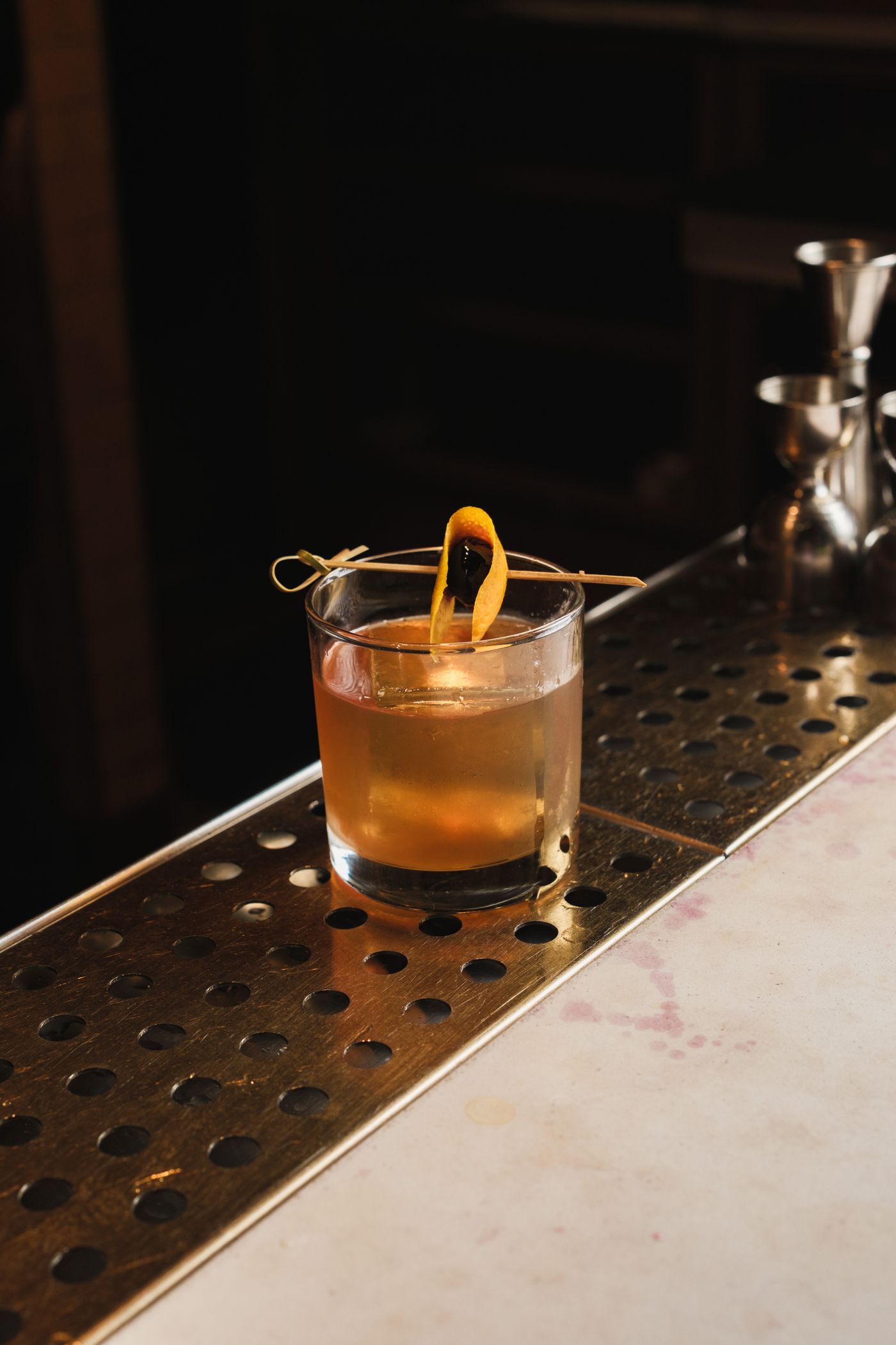 Old fashioned cocktail with a large ice cube and orange peel on a dark bar