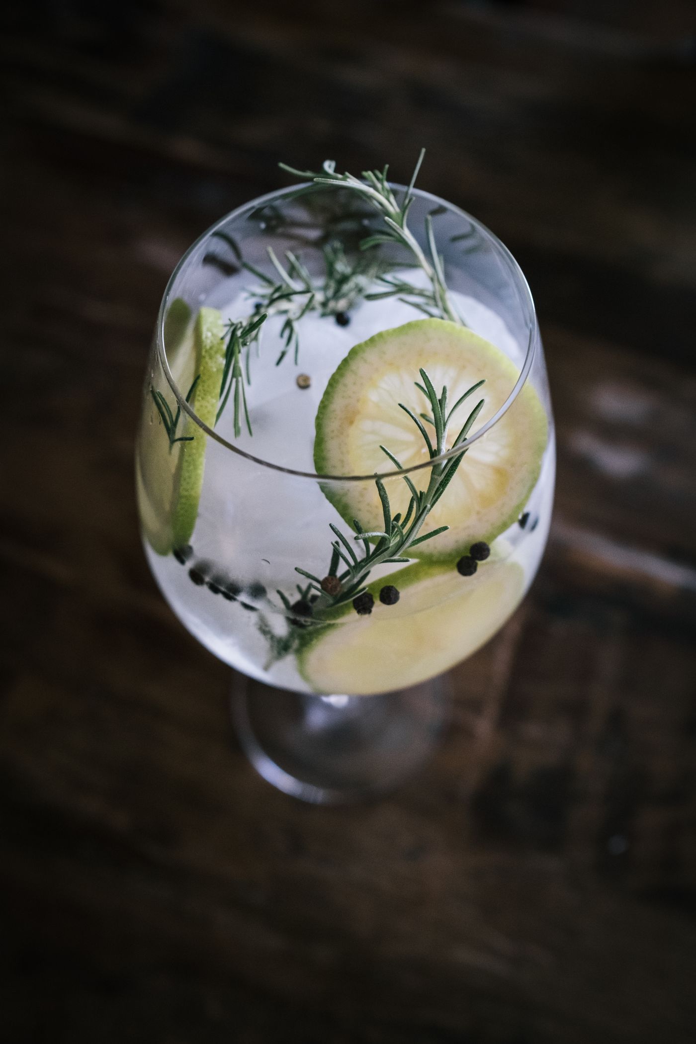 Gin and tonic in a balloon glass with lime, rosemary, and juniper on a dark table