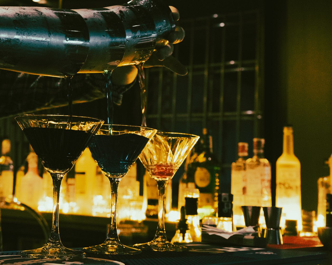 Cocktails being poured in a dim, golden-lit bar